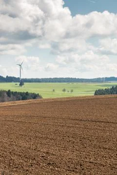 Big brown fields of fertile soil, green forest and wind power in the backgrou Stock Photos