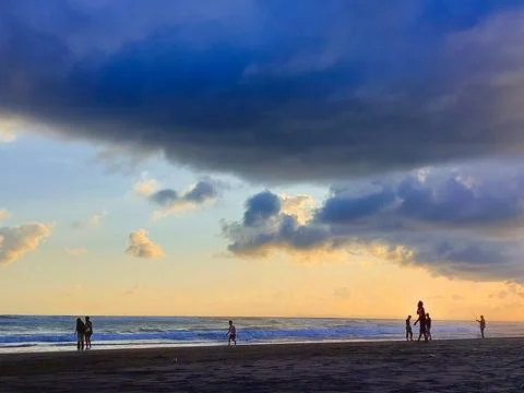 Big clouds hovering above beachgoers at golden hour Stock Photos