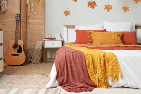 Big comfortable bed, bedside table and autumn decor in interior of bedroom Stock Photos