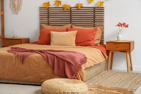 Big comfortable bed, bedside table, pouf and autumn decor in interior of styl Stock Photos