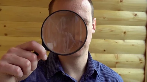 The big face of a curious man looking at the camera with a magnifying lens a Video stock 75814603