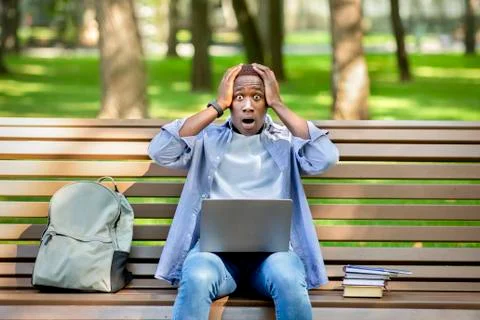Big failure. Young black guy holding his head in panic near laptop computer at Stock Photos