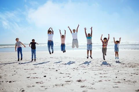 Big family, beach jump and adventure for holiday, sky and bonding for Stock Photos
