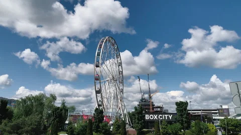 A big Ferris wheel against a backdrop of white clouds and green trees Stock Footage 242331752