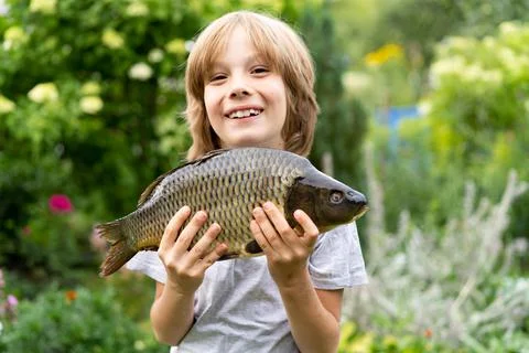 Big fish carp in the hands of a boy, fishing with a child, a young fisherman Foto stock