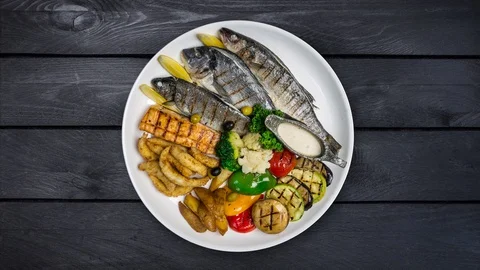 Big Fish platter rotating on a plate with vegetable. Black wooden background Stock Footage 128985979