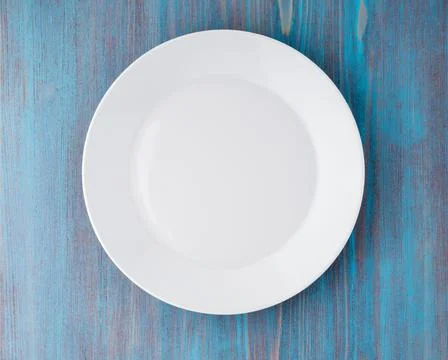 Big flat empty white plate on a blue wooden table, top view Stock Photos