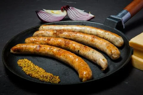 Big frying pan with fried thin sausages and granular mustard Фото