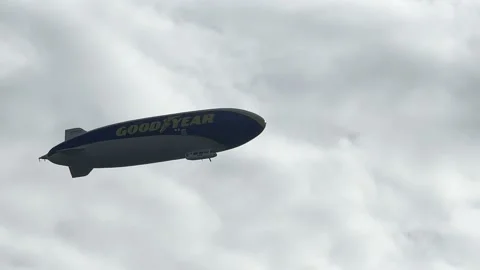 A big Goodyear blimp flying in a blue cloudy sky on the weekend. Zeppelin Stock Footage 201175619