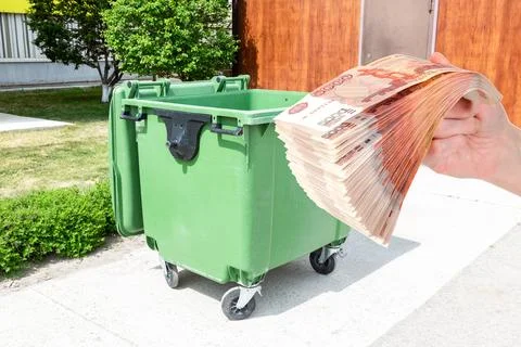 Big green plastic garbage container and stack of russian rubles in the hand Stock Photos