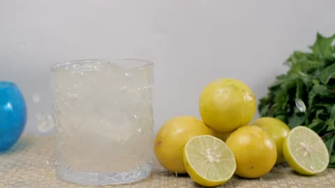Big ice cubes dropping in a glass of citrus refreshing lemonade placed on a t... Vídeo Stock 153070636