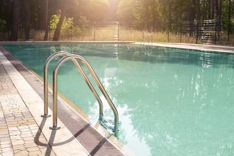 Big luxury empty rectangular swimming pool with clean blue water and ladder at Stock Photos