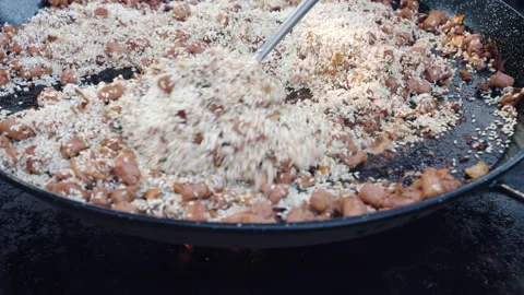 Big metal cauldron on burning fire, rice frying with sausages and chicken meat Stock-Footage 171949016