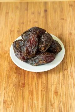 Big pitted dried dates on a small white plate set on a wooden boar top view Stock-Fotos