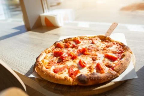 Big pizza stands on a table in a cafe. Italian pizza cut on pieces. Stock Photos