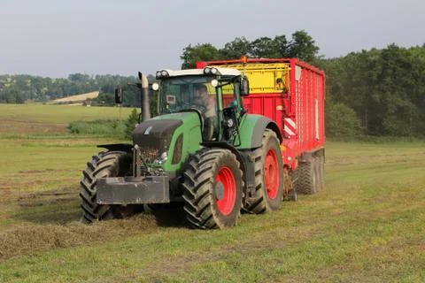 Big powerful tractor with attached self loading silage wagon picking up hay.. Stock Photos