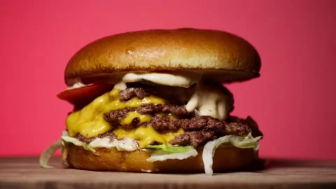 Big Quadruple Meat Cheeseburger Rotating on a Display on a Pink Background. Stock Footage 227227875