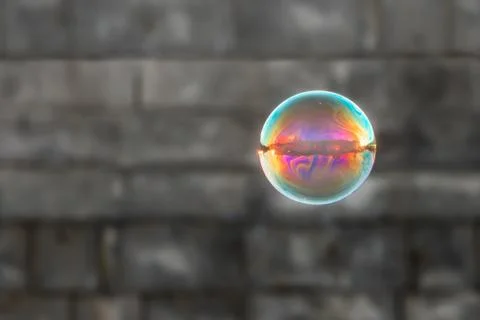 A big rainbow soap bubble on the blurred gray brick wall background Stock Photos