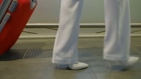Big red suitcase to roll on the arm of a woman in white shoes Video stock 71635388