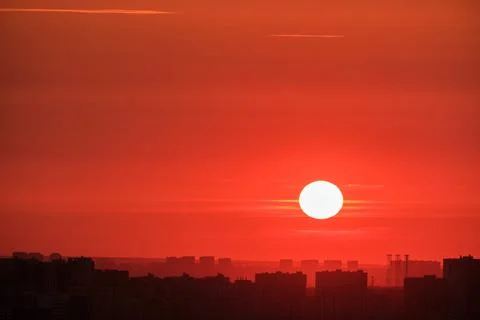 The big red sun sets behind the roofs of houses at sunset, timelapse Stock Photos