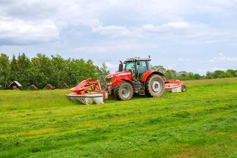Big red tractor with two mowers mows the grass for silage Stock Photos