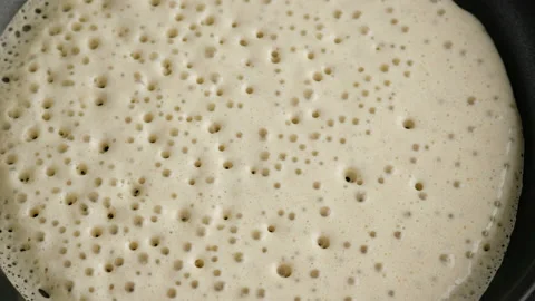 Big round pancake on induction frying pan. Cooking smoke goes up from pancake Stock Footage 145490614