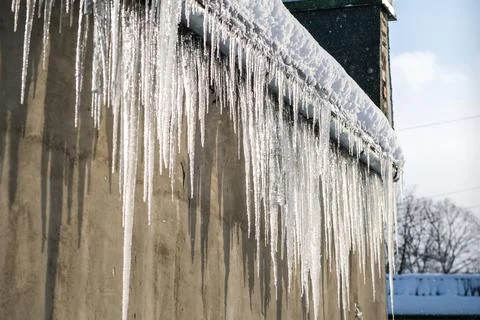 Big, sharp icicles and melted snow hanging from eaves of roof. Beautiful Stock Photos