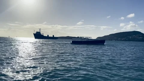 Big ship anchored offshore with a smaller boat moving nearby on calm blue water. 動画素材 336730468