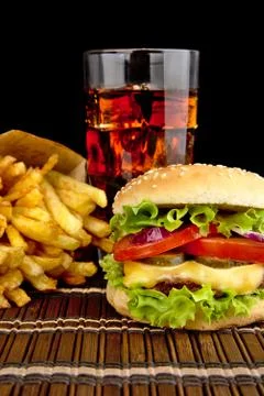 Big single cheeseburger with french fries with glass of cola on wooden mat on Stock Photos