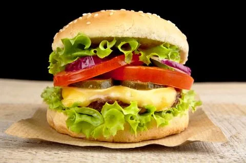 Big single cheeseburger on wooden board on black background Stock Photos