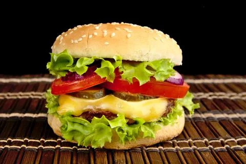 Big single cheeseburger on wooden mat on black background Stock Photos