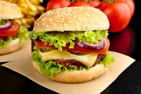 Big single cheeseburgers on paper on wooden black desk Stock Photos