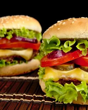 Big single cheeseburgers on wooden brown mat on black background Stock Photos