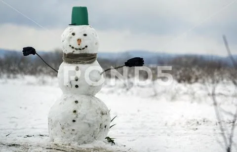 Big smiling snowman with bucket hat, scarf and gloves on white snowy field wi Stock Photos