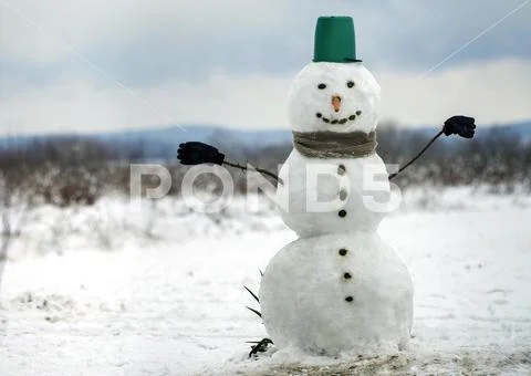 Big smiling snowman with bucket hat, scarf and gloves on white snowy field wi Stock Photos