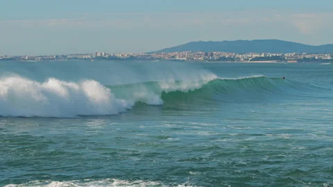 Big splashing ocean wave rushes towards the coast while people surfing Stock Footage 130628208