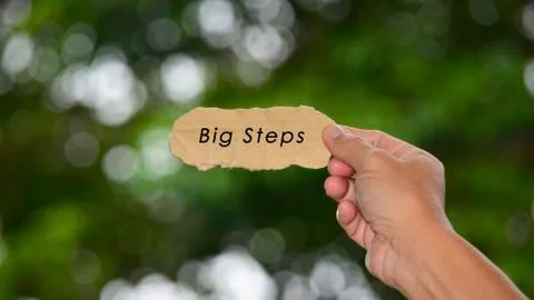 Big Steps Text On Hands Holding Torn Paper With Blurred Dark Background Stock Photos