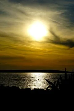 Big sun ball surrounded with clouds above shiny sea surface during the gold.. 库存照片