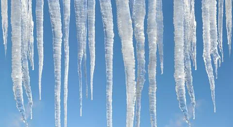 Big sunlit winter icicles on bright blue sky background Photos