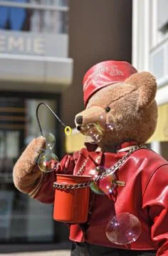 Big teddy bear with red hat and leather jacket blows soap bubbles in the air Stock Photos