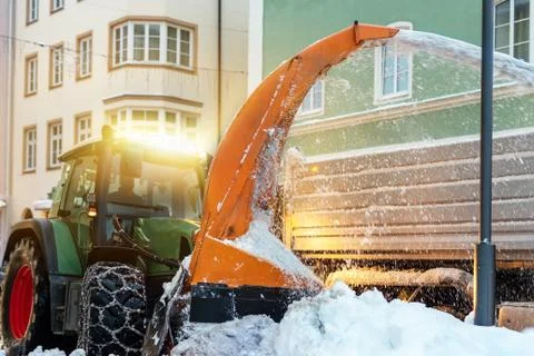 Big tractor with chains on wheel blowing snow from city street into dump truck 스톡 사진