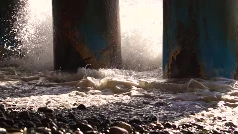 A big wave of the sun beats through rusty columns against the rocky beach Stock Footage 172280218