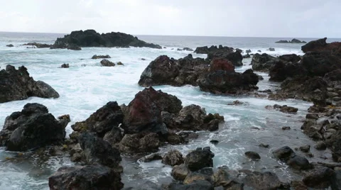 Big waves roll into and crash onto the volcanic rocks on the shore Stock Footage 64257844