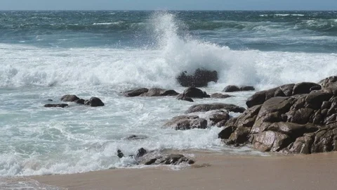 Big waves splash in slow motion on rocks on beach, throwing spray up into air. Stock Footage 115784533