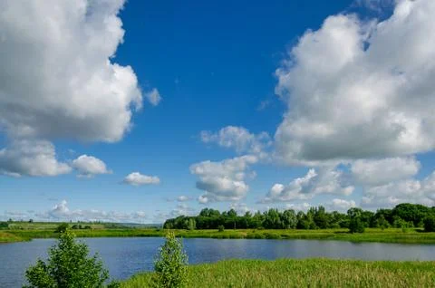 Big white clouds float over a lake in a forest on a blue sky, nature traveling Stock Photos