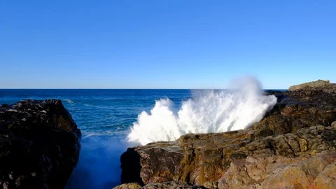 Big whitewater explosion with rainbow as wave crashes against cliff in rocky Vídeos de archivo 107780032