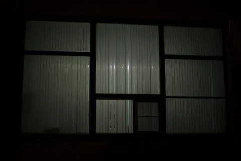 Big window at night. Window in building. Blinds cover light of lamp. Stock Photos
