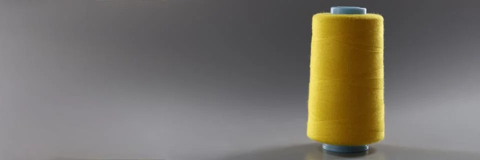 Big yellow bobbin of thin threads on a gray background Stock Photos