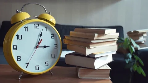 Big yellow clock is ticking while standing near the stack of books on the shelf Stock Footage 80814512