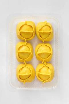 Big yellow dumplings Manti in plastic container for sale. Фото